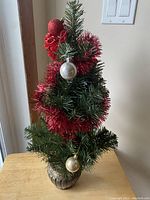 Full view of small artificial green holiday tree decorated with red tinsel and red, gold, and silver ball ornaments.