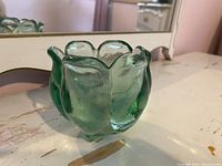 Small green glass vase or jar, approx. 4 inches tall, with petal-like rounded shape and textured surface seen from side angle.