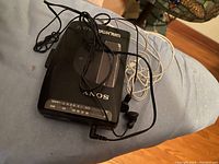 Sony Walkman cassette player with earbuds resting on surface, showing top side with Sony and Walkman logos.
