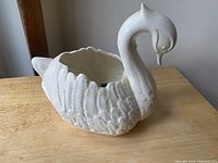 Photo of white ceramic swan figure from an angle showing detailed feather texture, curved neck, and hollow interior for use as a dish or flower pot.