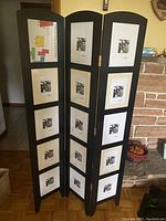 Front view of the black wooden three-panel room divider showing all photo frames with black and white floral prints.