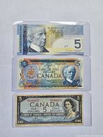 Front and back of three Canadian $5 bills from 2006, 1972, and 1954 in protective cases, showing portraits, security features, and serial numbers.