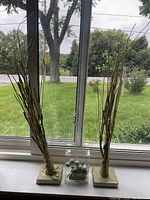 Two gold glitter coated decorative trees on square bases with visible battery wires near the base, placed on a windowsill with outdoor view.