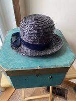Vintage woven ladies' Sunday hat with blue velvet band and bow on top of the teal octagonal vintage hat box.