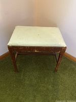 Angled side view of vintage wooden piano seat, showing cushion and wood finish with wear.