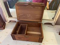 Open rectangular wooden jewelry box with hinged lid, showing exterior natural wood grain and decorative grooved corner details.