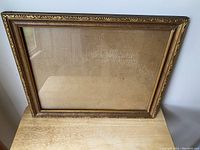 Front view of vintage picture frame with gold-toned metal leaf-embossed border and glass pane.