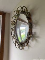 Side angled view showing the metal floral decorative border around the round mirror and its thickness