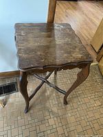 Front side angle view of vintage wooden side table showing scalloped edge top, curved legs with decorative carving, and wear on surface.