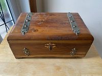 Front view of wooden jewelry box showing metal hinges on lid and front latch, surface wear visible