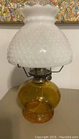 Hurricane lamp with amber glass base and white hobnail milk glass shade on top.
