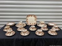 Full set displayed on a black cloth with all cups, saucers, plates, and pitcher arranged.