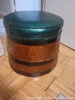 Green leather covered barrel stool with wooden barrel base and black metal bands around it, shown in two angles.