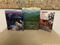 Three hardcover books on Canada displayed together: Mountains of Canada, Historical Atlas of Canada, and The Contemporary Atlas of Canada and the World.