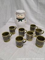 Photo of 8 brown geometric patterned ceramic mugs surrounding the pig chef cookie jar.