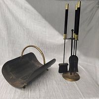 A side view of the ash shovel and the fireplace tool stand holding four tools (broom, poker, shovel, tongs) with black bodies and gold accents.