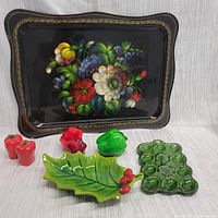 Detailed view of hand painted floral tray alongside assorted ceramic shakers, green deviled egg tray and holly leaf dish