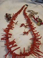Photo showing coral necklace, amber pendant, and two antique brooches arranged on a white cloth.