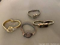 Four vintage ladies wristwatches arranged on flat surface, showing varied shapes and metal tones.