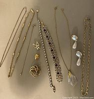 Top view showing assorted chains, bracelets, brooches, earrings arranged on neutral surface