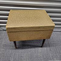 Full front view of the mid century sewing stool showing the vinyl fabric and wooden legs in overall good condition.