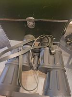 Tasco 8x40 camouflage binoculars with textured grips and neck strap, placed in front of the green hard case.