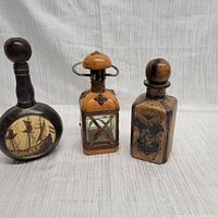 Photo showing set of three vintage leather wrapped decanters with different shapes and designs
