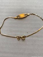 Photo showing front of yellow gold ID bracelet with engraved leaf-like designs on the ID plate and spring ring clasp