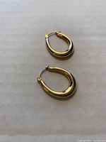 Top view of the pair of hollow oval hoop earrings lying on a white surface, showing shiny yellow gold color and puffed shape