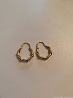 Pair of gold small hoop earrings with nautical rope design, laid flat on a surface.