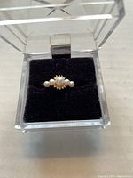 Top view of an 18Kt gold ring with five pearls displayed in a clear jewelry box with black velvet interior.