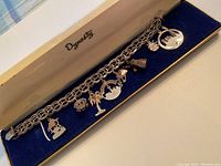 Sterling silver chain bracelet with 8 various charms including castle, mushroom, horse, tree, bell, and other detailed charms in blue velvet case with Dynasty logo.