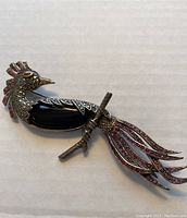 Side view showing the shape and gemstone inlays of the peacock brooch on a light surface.