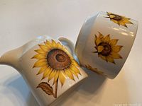 Close-up of cream pitcher and sugar bowl showing sunflower decoration and ceramic finish.