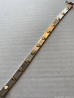 Full view of the flat sterling silver bracelet with round gold tone rivet details evenly spaced along length.
