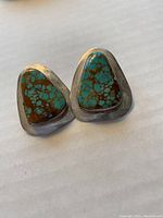 Pair of large sterling silver earrings with turquoise triangular stones set in bezels, showing brown matrix veining.