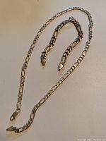 Full view of silver necklace and bracelet laid on flat surface, showing necklace with clasp and bracelet with open links.