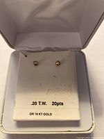 Pair of earrings displayed in white presentation box, showing front view of stones and card