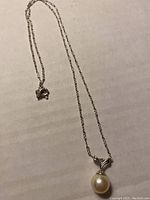 Photo of the delicate silver necklace chain with a white pearly bead pendant, laid flat showing clasp and pendant.