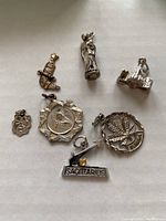 Photo showing all seven silver charms arranged on a white background, clear details of each charm, including inscriptions and designs.