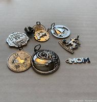 Lot of 9 various sterling silver charms arranged on a flat surface, visible details include zodiac signs, lettering, and decorative charms.