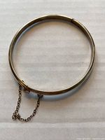 Top-down view of the silver hinged bangle with attached safety chain, showing the smooth circular shape and clasp area.