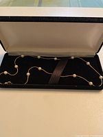 16 inch sterling silver chain necklace with 11 white pearl beads spaced evenly along chain, laid in a jewelry box with black velvet interior.