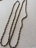 Two long twisted silver chains laid flat on cardboard showing their full length and twisting link design.