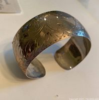 Angled side view showing the engraved pattern on the wide sterling cuff bracelet and its open adjustable back.