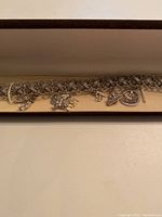 Sterling silver woven charm bracelet displayed inside a beige jewelry box showing six unique charms attached to the chunky woven chain.