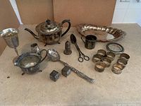 All items spread out and visible on countertop showing detail of main silver pieces including teapot, tray, napkin rings, and serving utensils.