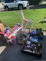 View of wireframe reindeer decoration, plastic tote with assorted wrapping paper rolls, boxes with Christmas cards, and assorted decorations arranged on the ground