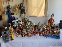 Wide view of table covered with many clown-themed collectibles including dolls, marionettes, and figurines.