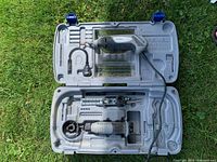 Photo showing open carrying case with two rotary tools, flexible shaft, and saw attachment inside case compartments, placed on grass.